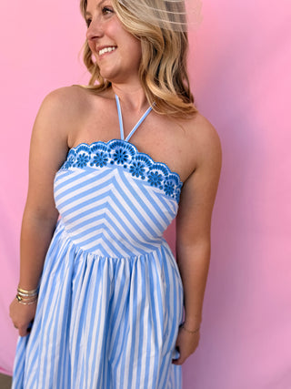 Woman wearing a blue and white striped dress with floral details against a pink background