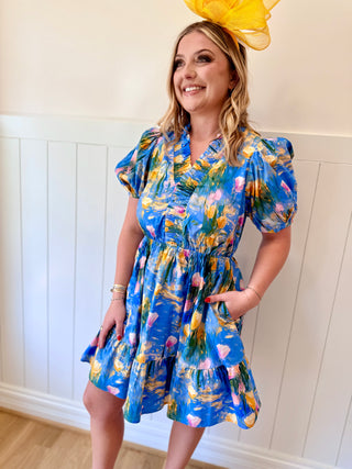 Woman wearing a blue floral dress with a yellow hat indoors.