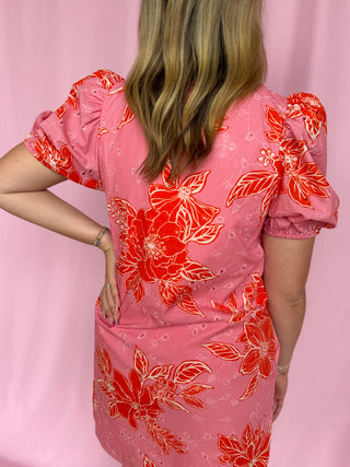 Person wearing a pink dress with red floral pattern against a pink background