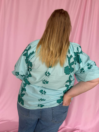 Person wearing a light blue blouse with green floral patterns against a pink background