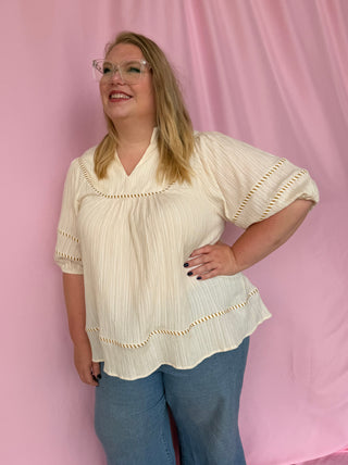 Woman wearing a white blouse with short sleeves and blue pants against a pink background