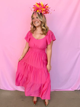 Woman wearing a pink dress and floral headpiece against a pink background