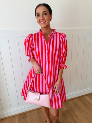 Woman wearing a red and white striped dress holding a pink handbag indoors.