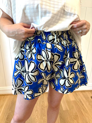 Person wearing a white shirt and blue floral shorts indoors.