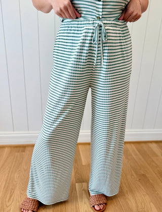 Person wearing a striped outfit with wide-leg pants against a white paneled wall.
