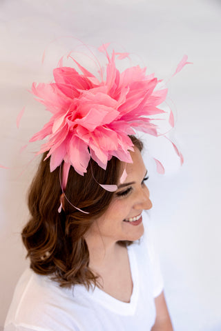Woman wearing a large pink feathered headpiece against a white background