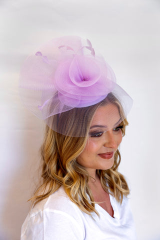 Woman wearing a light purple fascinator with a veil on a white background