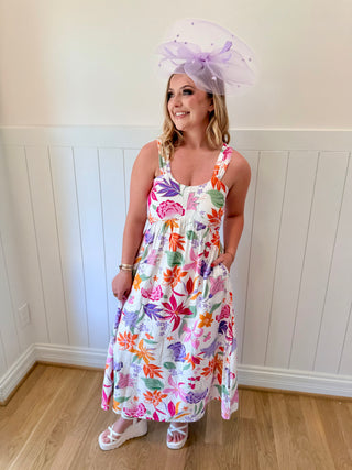 Woman wearing a colorful floral dress and a large decorative hat indoors.