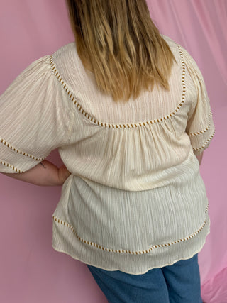 Person wearing a beige blouse with decorative trim against a pink background
