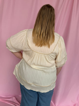 Person wearing a beige blouse with lace details against a pink background
