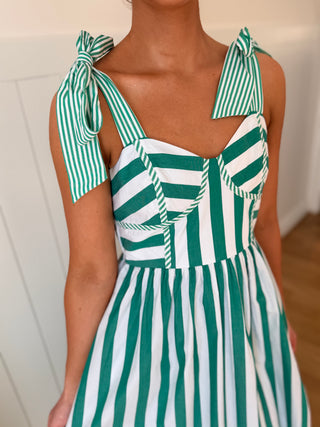 Green and white striped dress with bow straps on a neutral background