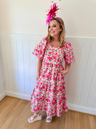 Woman wearing a pink floral dress and a large pink feathered headpiece indoors.