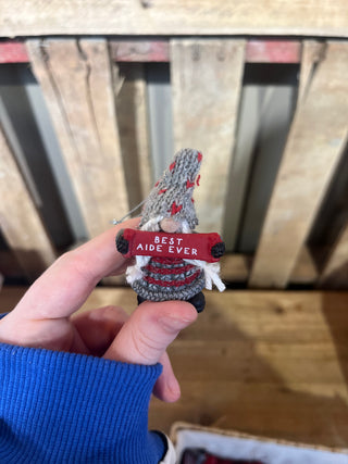 Hand holding a small red and gray object with 'Best Ape Ever' text against a wooden background