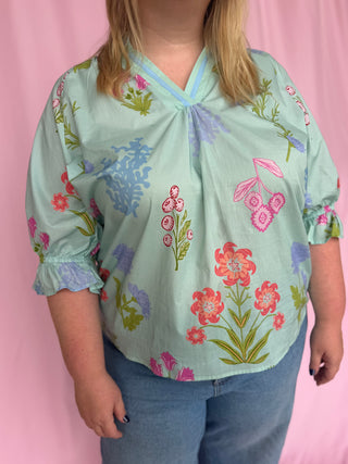 Person wearing a light blue floral blouse against a pink background