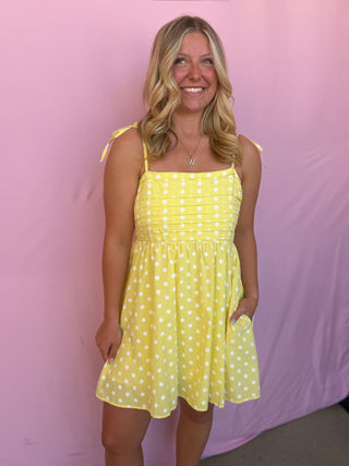 Woman wearing a yellow polka dot dress against a pink background