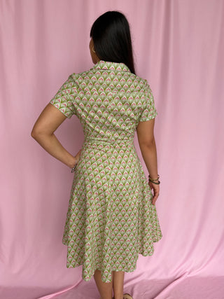 Woman wearing a green patterned dress against a pink curtain background