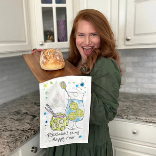 Woman holding a loaf of bread and a towel with pickleball design in a kitchen.