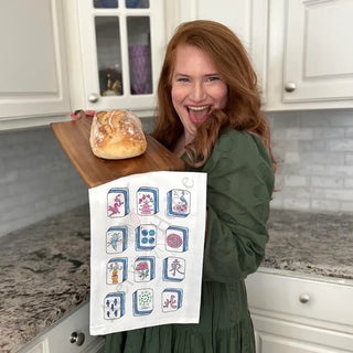 Woman holding a loaf of bread on a wooden board with a decorative towel in a kitchen.