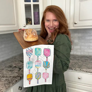 Woman holding a loaf of bread on a wooden board with a colorful towel featuring ice cream illustrations in a kitchen.