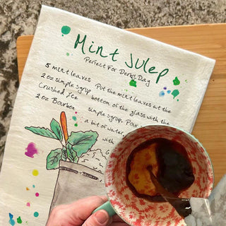 Napkin with Mint Julep recipe and a cup of mint julep on a wooden surface