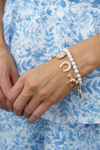 Close-up of a wrist wearing multiple bracelets with charms against a blue floral background