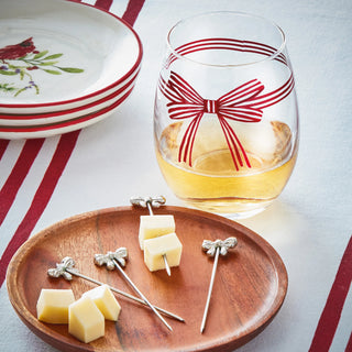 Glass with a red bow design, cheese on skewers, and plates on a tablecloth.