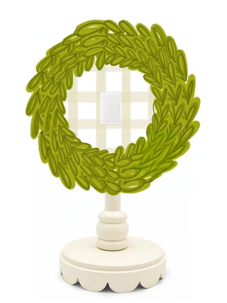 A decorative tabletop mirror with an olive green laurel wreath frame and a cream-colored pedestal stand, shown against a plain white background.