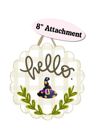 A Halloween-themed decorative hanging sign with a scalloped cream border, a pink gingham background, the word 'hello' in dark brown script, a small witch hat illustration, green leafy branches, and a pink oval label above reading '8" Attachment'.