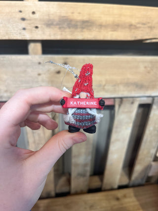 Hand holding a small figurine with a red name tag labeled 'Katherine' against a wooden background.