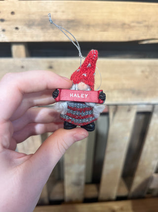 Hand holding a small crocheted ornament with 'Haley' on a wooden surface