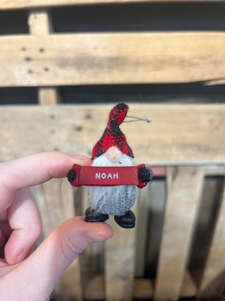 Small gnome figurine with a red hat and 'NOAH' tag held by a hand against a wooden background
