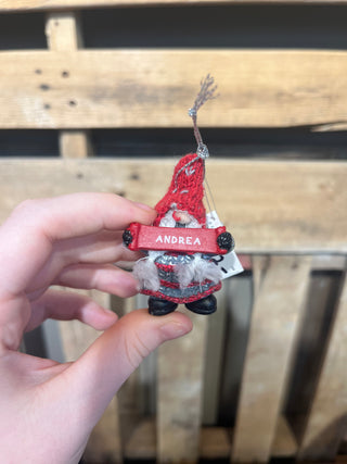 Small gnome ornament with a red hat and 'Andrea' tag held by a hand against a wooden background