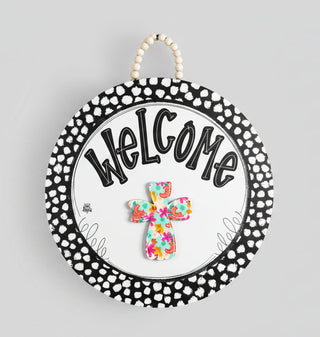 Decorative sign with 'Welcome' text and a colorful cross on a polka dot background.