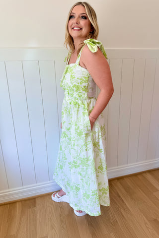 Woman wearing a white dress with green floral patterns indoors.