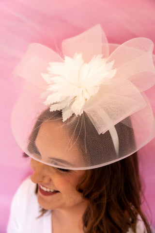 Person wearing a pink headpiece with a white flower against a pink background