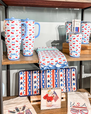 Display of patriotic-themed products including mugs, towels, and coasters on a wooden shelf.