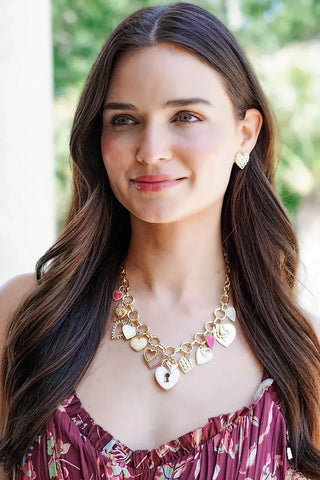 Woman wearing a floral dress and gold necklace with heart pendants outdoors.