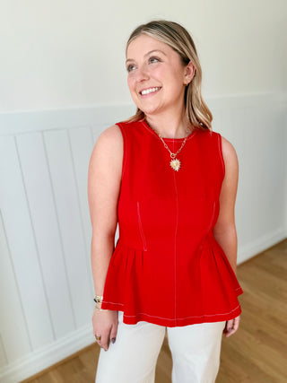 Woman wearing a red sleeveless top and white pants indoors.