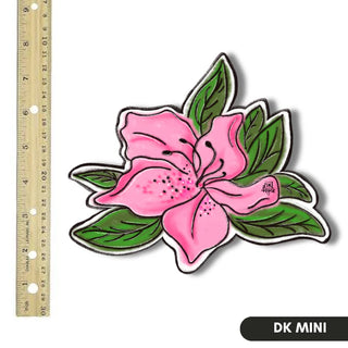 Pink flower sticker with green leaves next to a ruler on a white background