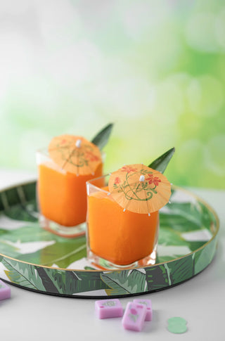 Two glasses of orange juice with decorative umbrellas on a green leaf-patterned tray.