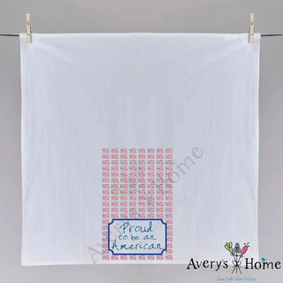 White towel with 'Proud to be an American' text and flag pattern, hanging on a gray wall.