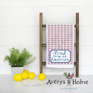 White towel with 'Proud to be an American' text on a wooden ladder against a white wall, with 'Avery's Home' branding.