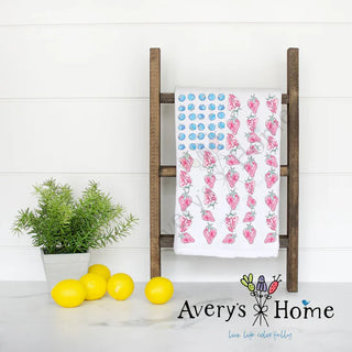 Wooden ladder with a towel featuring strawberry pattern, lemons, and a plant on a white background with 'Avery's Home' branding.