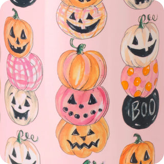A close-up of a pink patterned surface featuring illustrated jack-o'-lantern pumpkins stacked vertically in orange, pink, cream, and black, with the word BOO on one pumpkin.