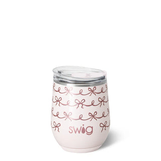 A pale pink insulated stemless wine tumbler with a clear lid, decorated with rose gold bow patterns and the 'swig' logo, shown on a white background.