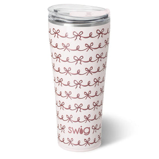 A tall white insulated tumbler with a clear lid, decorated with a repeating dusty rose bow pattern and the word 'swig' near the bottom, shown on a white background.