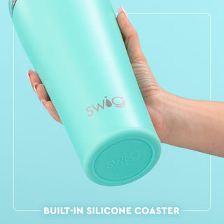 Turquoise Swig tumbler with built-in silicone coaster held by a hand on a light blue background