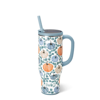 A tall insulated travel tumbler with a handle and straw, featuring a white background with an autumn pumpkin pattern in orange, blue, and beige. The handle and lid are light blue, and the word 'swig' is printed near the bottom.