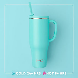 A light turquoise insulated travel tumbler with a matching handle, lid, and straw, shown on a matching light blue background. The tumbler has a silver metallic rim and the brand name 'swig' printed near the bottom.