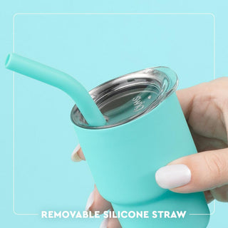 Turquoise tumbler with a removable silicone straw held by a hand against a light blue background.